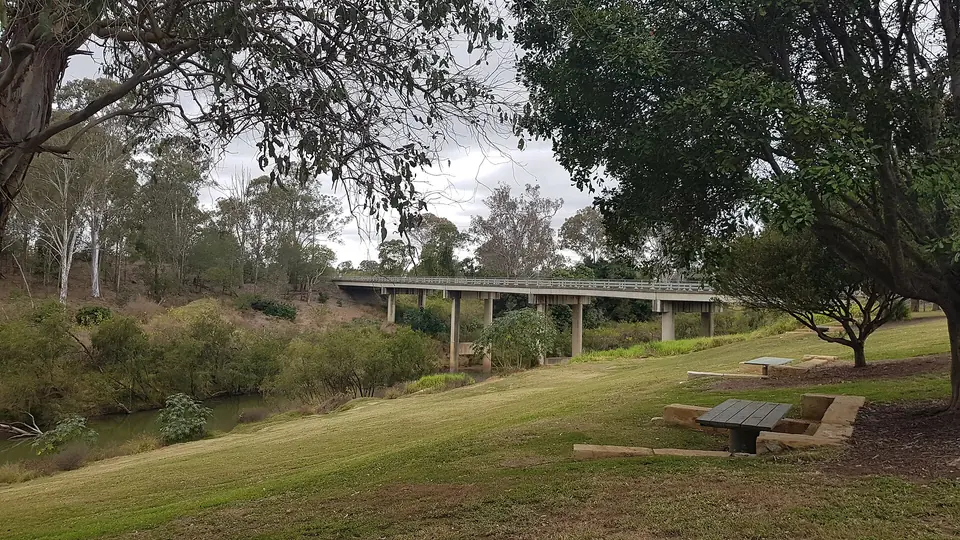 A grassy slope with picnic tables at Lions Riverside Park, with the river bridge behind the trees.